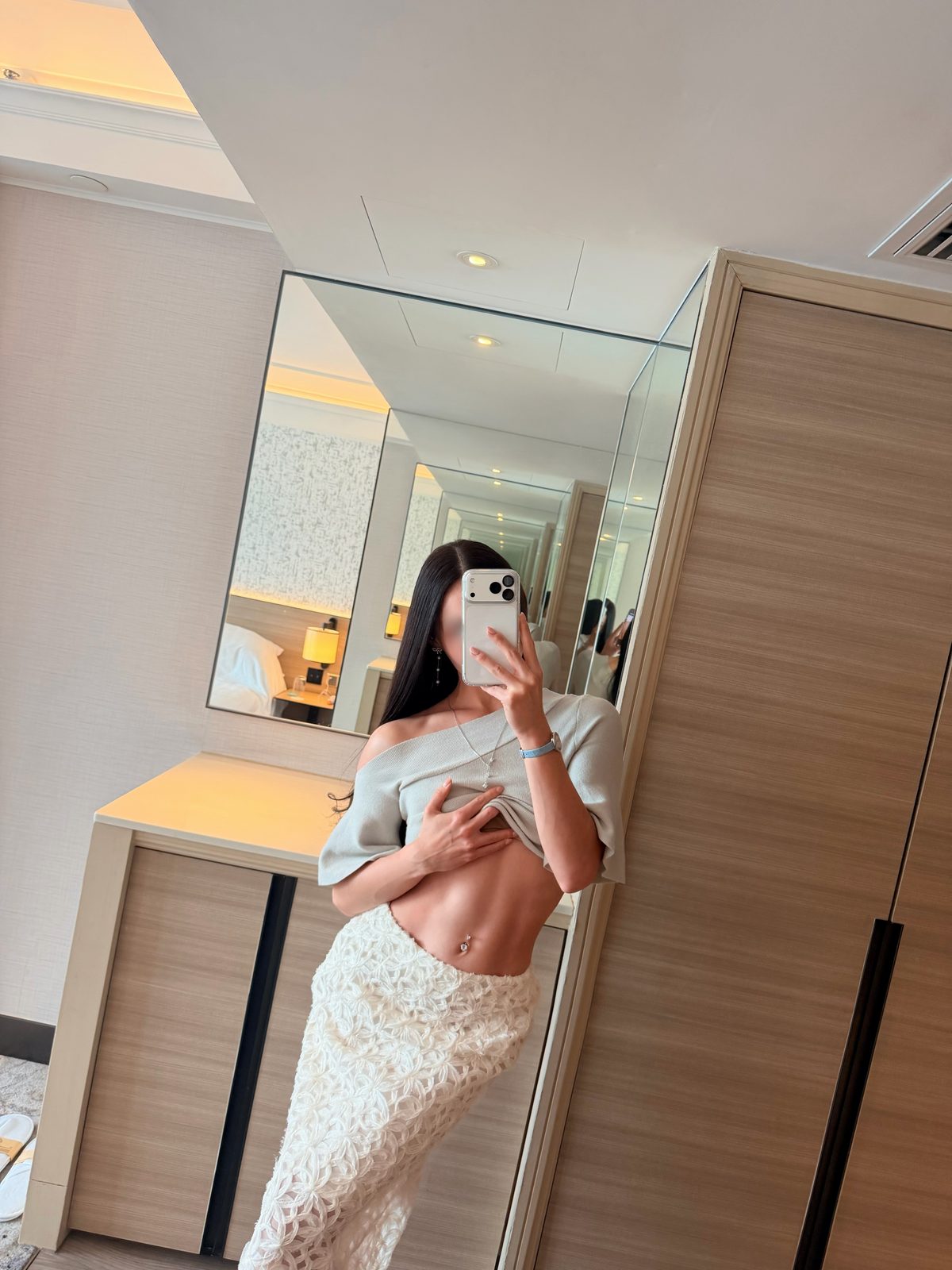 Irina, a mirror selfie in a sage knit top and white crochet skirt beside a dressing table in a softly lit suite