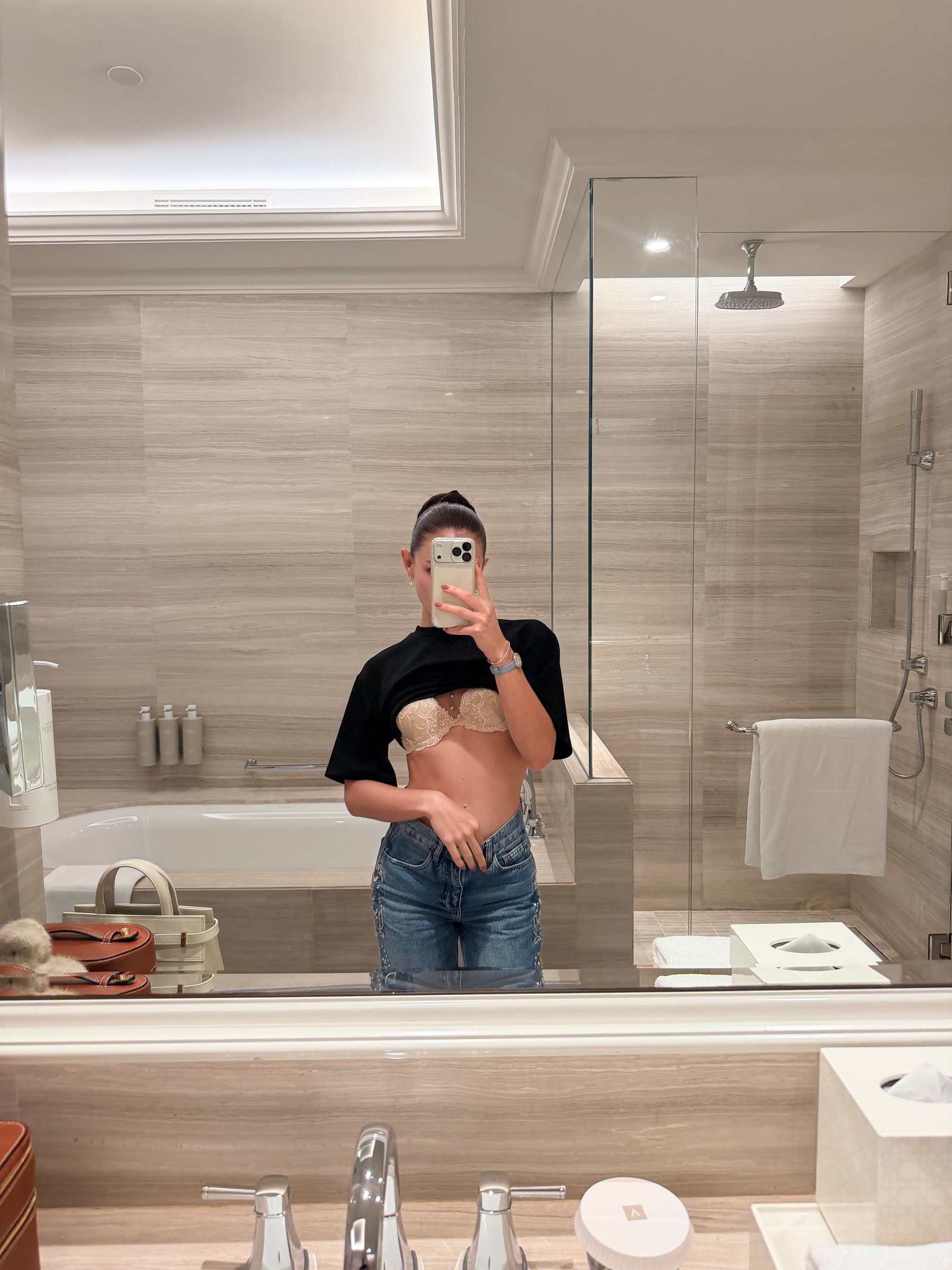 Irina, a mirror selfie in denim jeans, a black cropped top and ivory lace in a marble bathroom