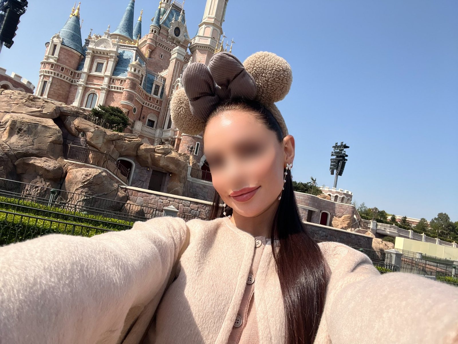 Irina, a playful day-out selfie in Minnie ears and a camel coat before a fairytale castle