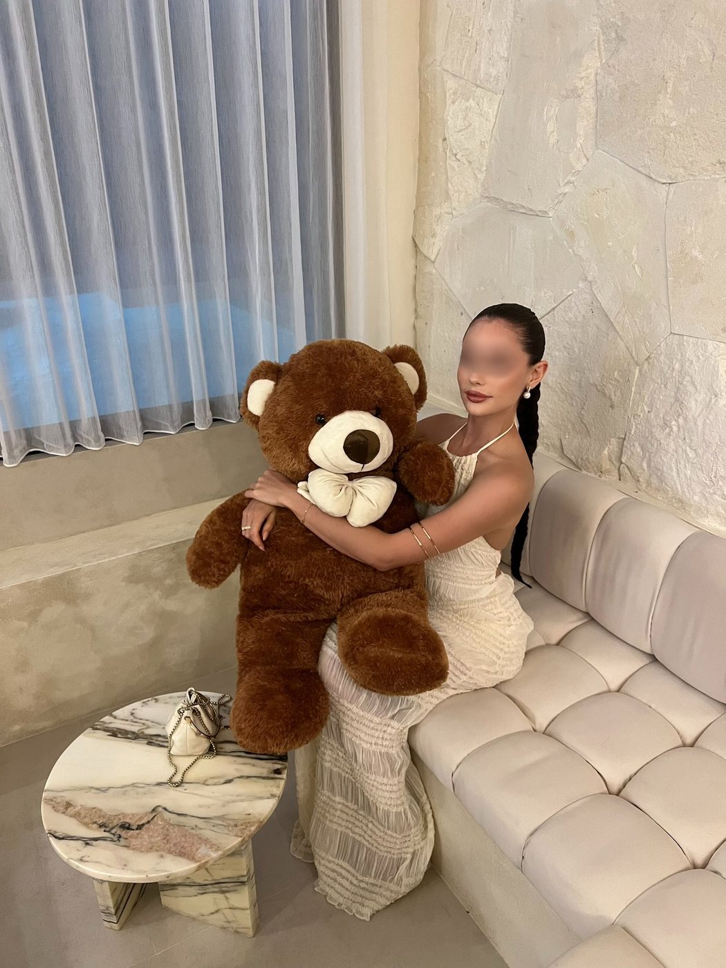 Irina, an off-duty selfie in a cream gown holding an oversized teddy bear at home