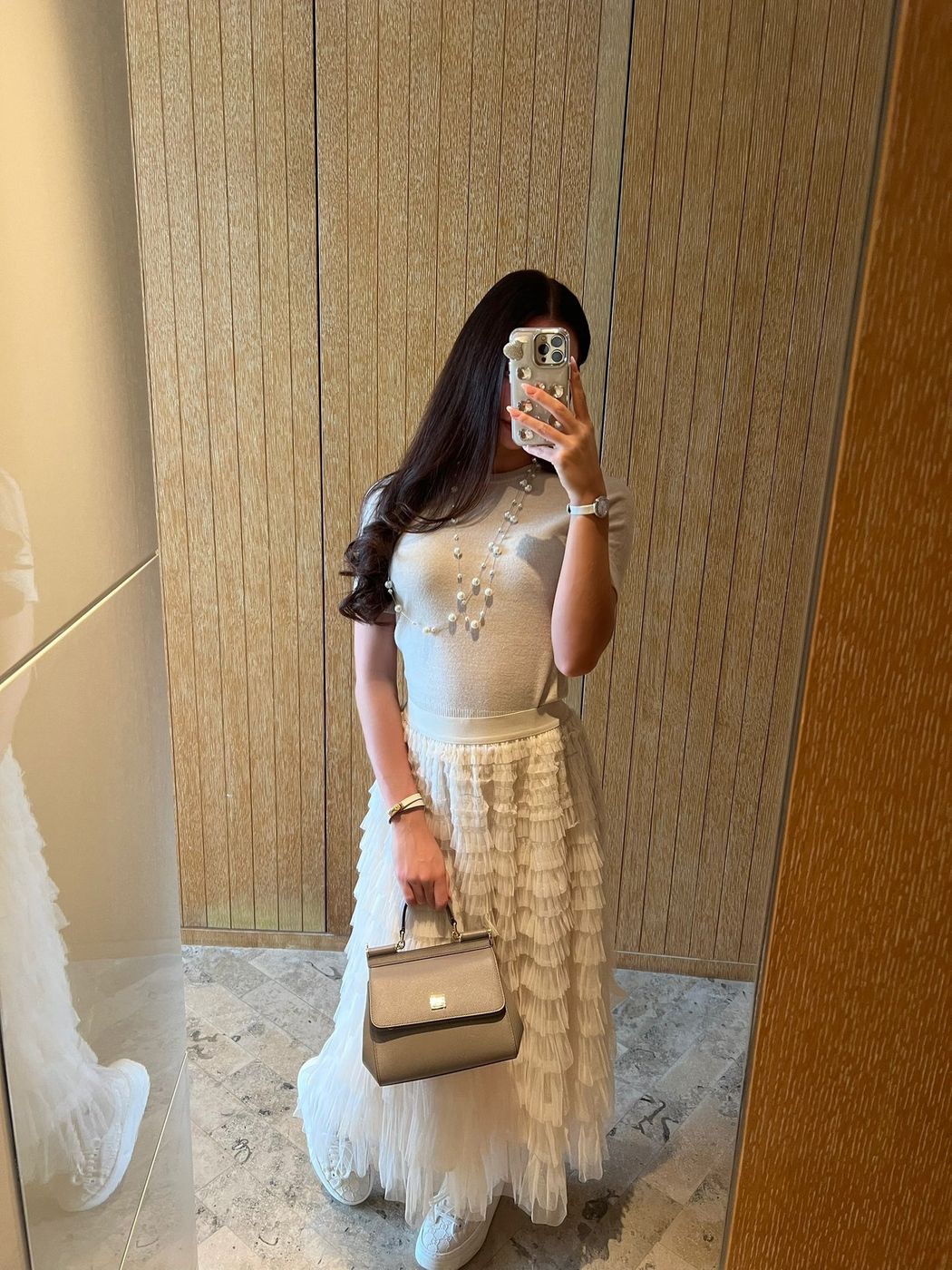 Irina, a fitting-room mirror selfie in a white knit top and tiered tulle skirt with a taupe top-handle bag
